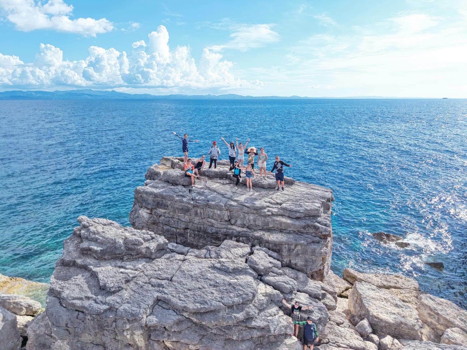 Guests on a rocky headland above the deep-blue sea on a Ticao island-hopping trip off Masbate
